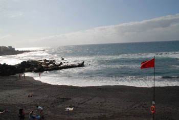 Red beach flag on black Tenerife beach.